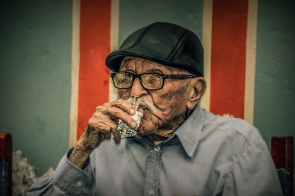 An old man in a cap drinking vodka