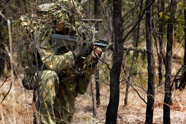 Sniper in camouflage uniform with a machine gun in the forest