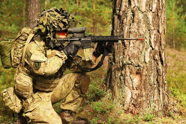 Un soldado se sienta detrás de un gran árbol con un arma en un pelotón