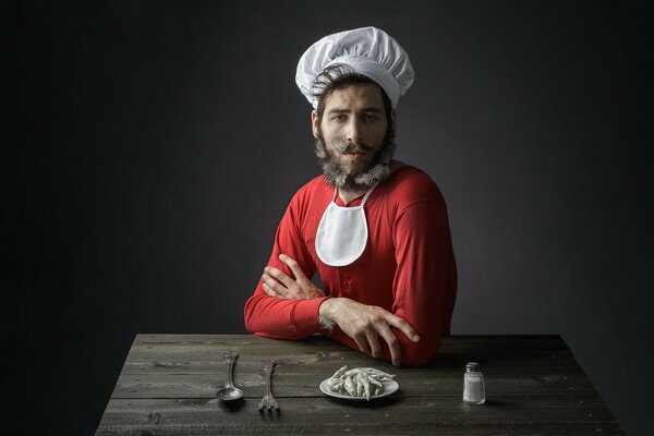 A man sitting at a wooden table, dressed as a cook