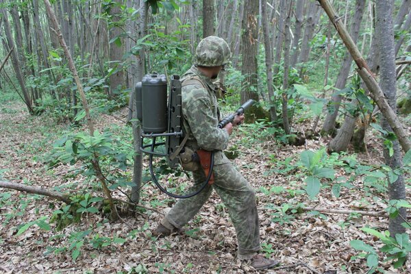 A man in camouflage, in the forest with a flamethrower