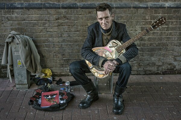 Uomo con una chitarra contro un muro di mattoni