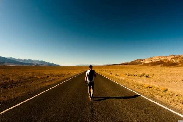 A man walks along a road in the desert