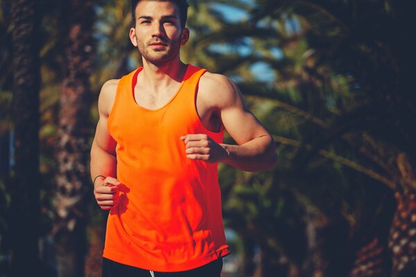 A man in an orange T-shirt runs through the park