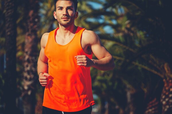 Mężczyzna w pomarańczowej koszulce biegnie po parku