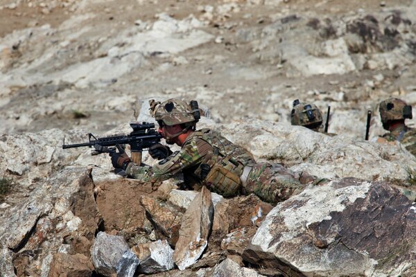 An American soldier lies and looks through the sight in the rocks