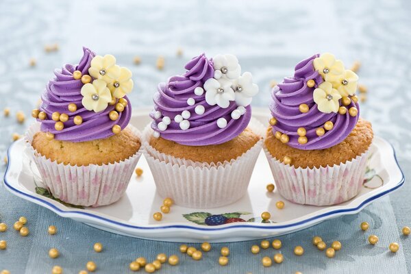 Three cupcakes on a plate with purple cream and flowers