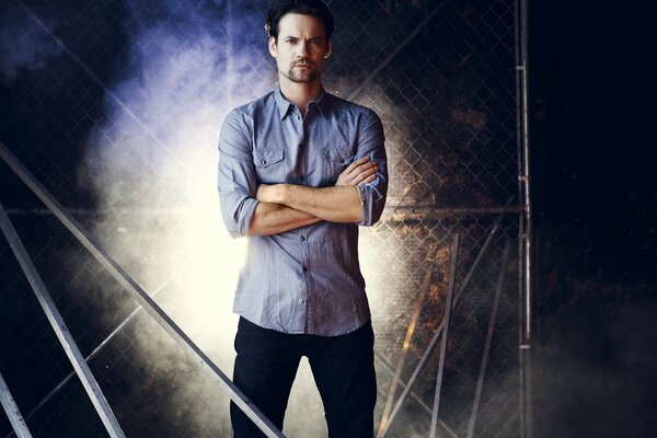 Shane West en una camisa azul sobre un fondo de celosía