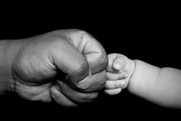 The hand of a man and a baby on a black background