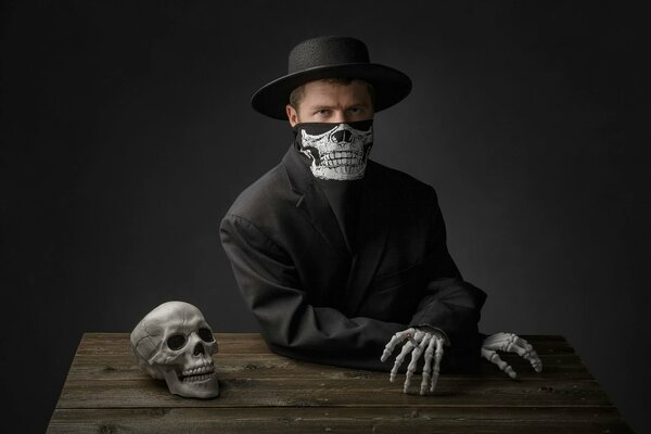 A man in a black suit at a table with a skull