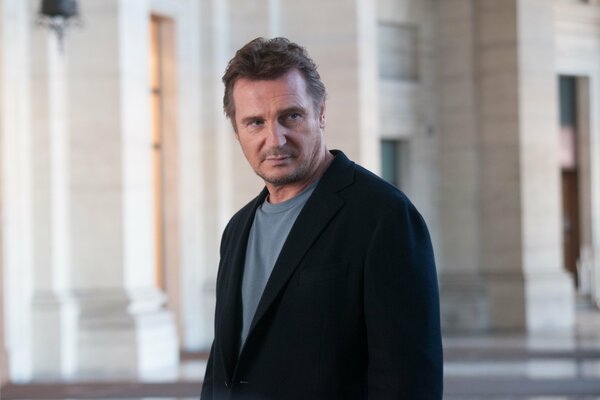 Liam Neeson stands in the middle of the street