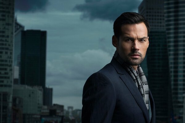 A handsome man looks into the camera lens against the background of urban structures