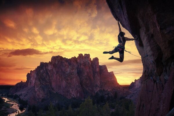 The climber is hanging on a cliff on one hand