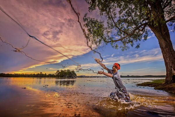 Un pescador lanza una red, en un río al atardecer