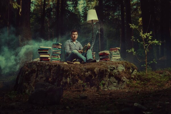 A book lover sits in the middle of the forest with books and a lamp