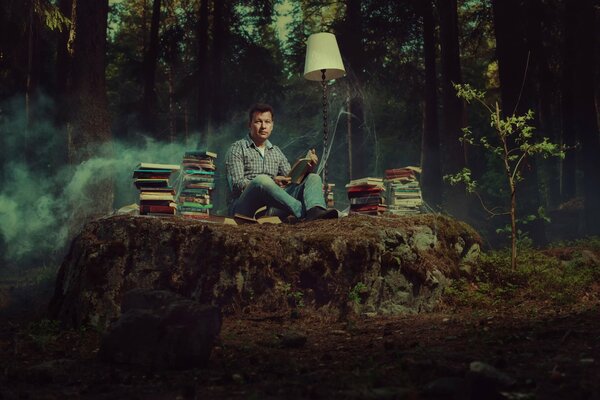 Un amante de los libros se sienta en medio de un bosque con libros y una lámpara