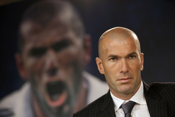 Zinedine Zidane in giacca e cravatta sullo sfondo della sua foto