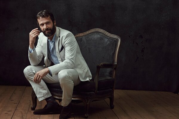 James Purfoy en costume blanc est assis dans une chaise