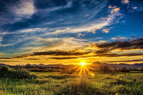 Bei Sonnenuntergang umhüllen die Sonnenstrahlen das Feld und die Berge