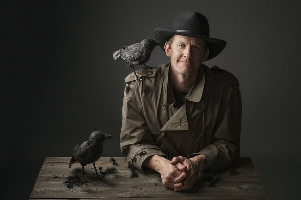 A man in a hat with a crow on his shoulder