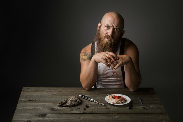 A bearded man sits at a table and eats