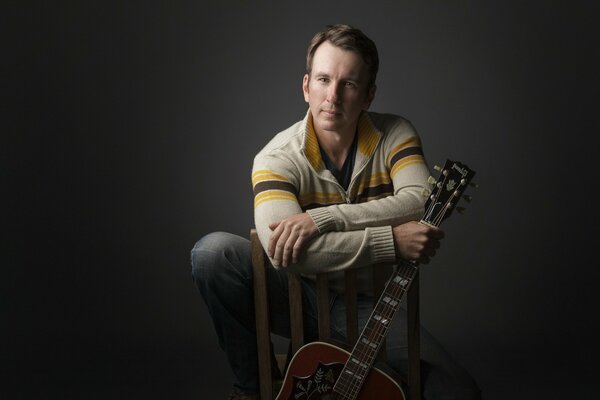 Jason Burton avec une guitare sur une chaise