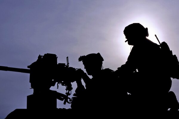 Silhouettes of two soldiers and a machine gun against the sky