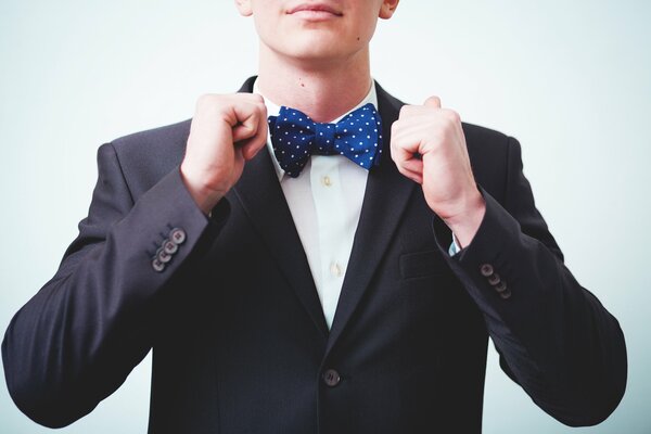 The groom puts on a blue bow tie with a black suit