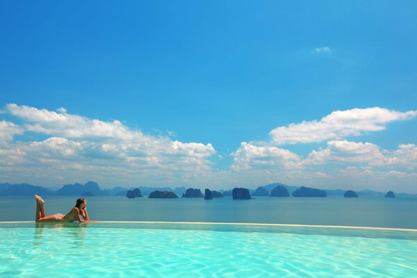 A girl in a swimsuit against the background of the sky and a large pool