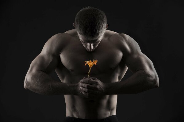 Ein Mann mit aufgepumpten Muskeln hält eine Lilie