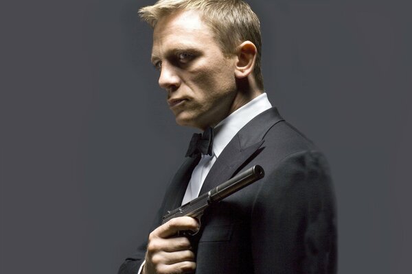 Aktor Daniel Craig, który grał Jamesa Bonda, z pistoletem w ręku na szarym tle