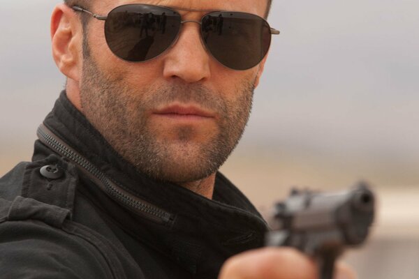 Jason Statham trägt eine Brille mit einer Pistole