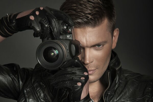 A hot guy in a leather jacket and gloves with a mirror in his hands