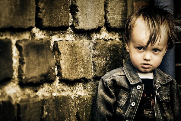 Un niño está de pie junto a una pared de ladrillo