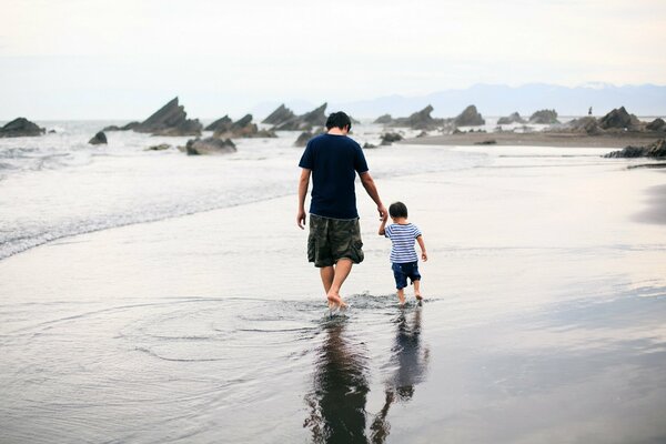 Passeggiata dell uomo con il figlio indietro sulla riva del mare