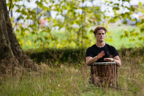 Ein Mann mit einer Trommel spielt neben einem Baum