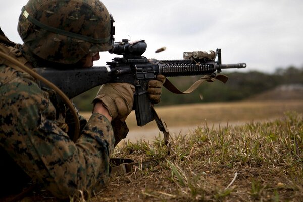 A soldier shoots from a machine gun lying on the grass