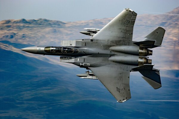 A military plane is flying over a mountainous area