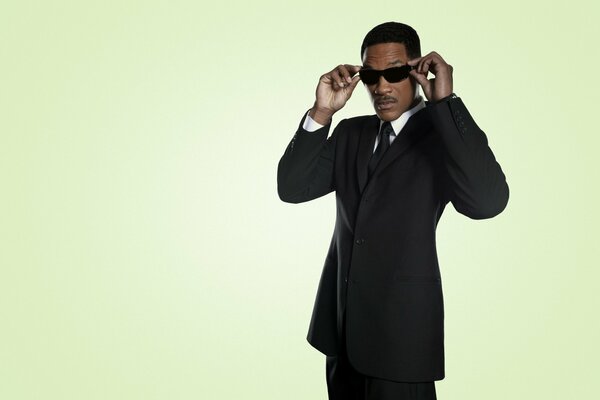 Homme à la peau foncée dans des lunettes noires et costume posant mystérieusement sur fond vert