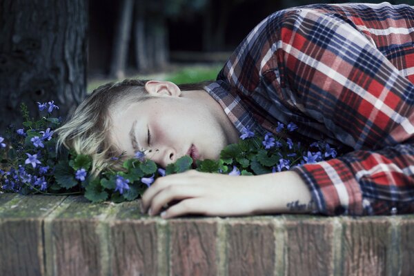 El chico que duerme entre violetas bajo un árbol