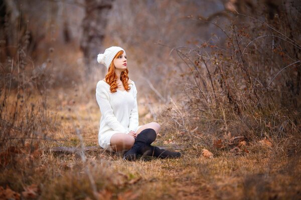 Ruda dziewczyna z białą czapką i swetrem w środku jesiennego lasu