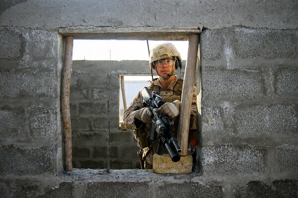 Photo of a soldier with a gun in his hands against the background of brick walls