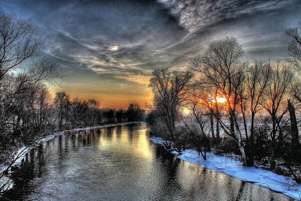 Winter Sonnenuntergang auf dem Hintergrund von Bäumen, Fluss mit Schnee