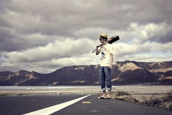 A guy with a guitar is standing on the road