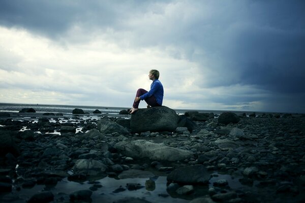 Facet siedzący na skałach i wpatrujący się w morze