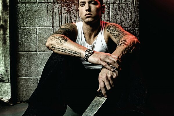 Rapper Eminem with a huge knife is sitting on the floor against a stone wall