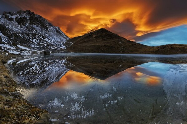 A mountain covered with snow by a lake at sunset