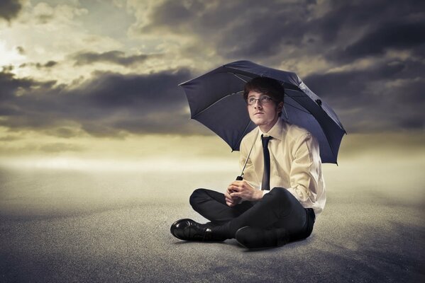 Ein Mann sitzt im Anzug im Sand unter einem Regenschirm