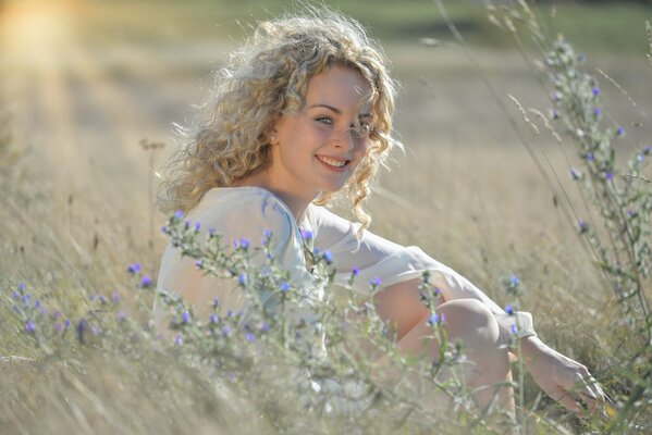 Blonde bouclée avec un sourire assis dans un champ