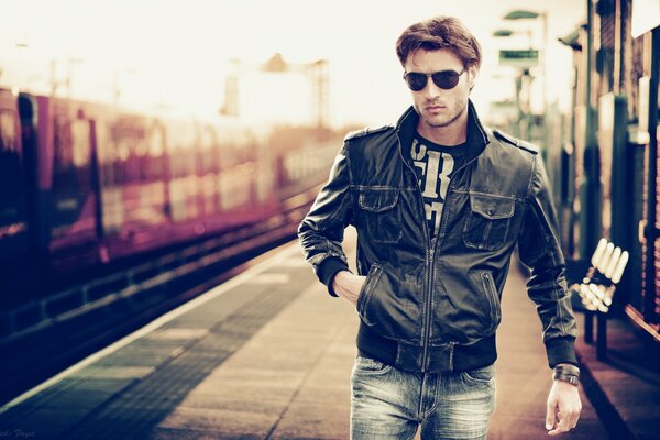 A man in glasses and a leather jacket at the train station